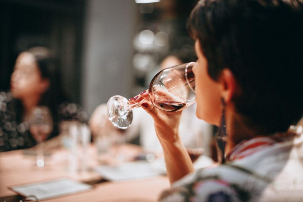 Woman drinking a glass of wine with friends at a softly lit table, capturing the relaxed feeling of social drinking before the stress rebound sets in.